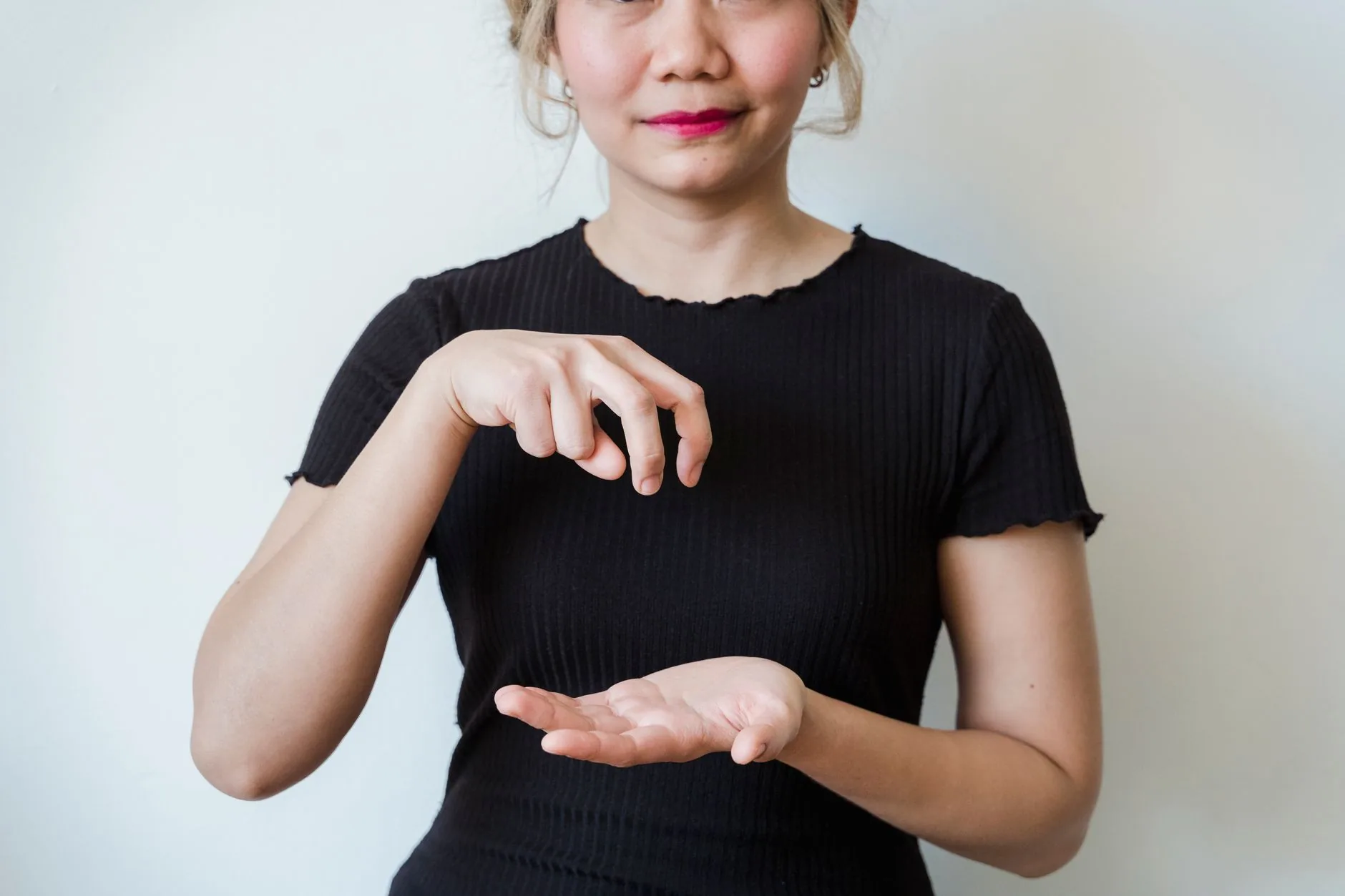 Femme en haut noir faisant un geste des mains devant un fond blanc