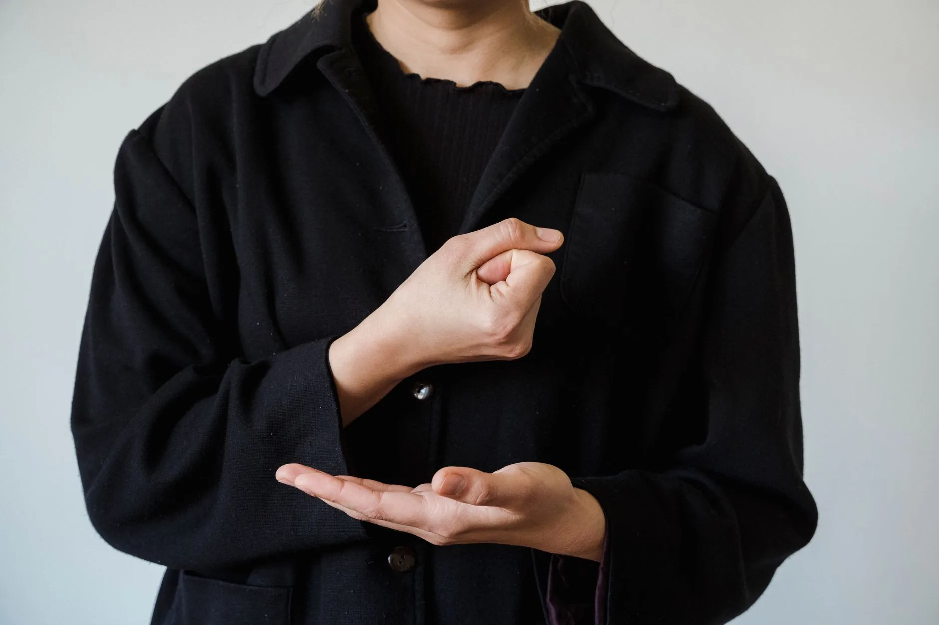 Personne en manteau noir formant un signe de langue des signes devant un mur gris