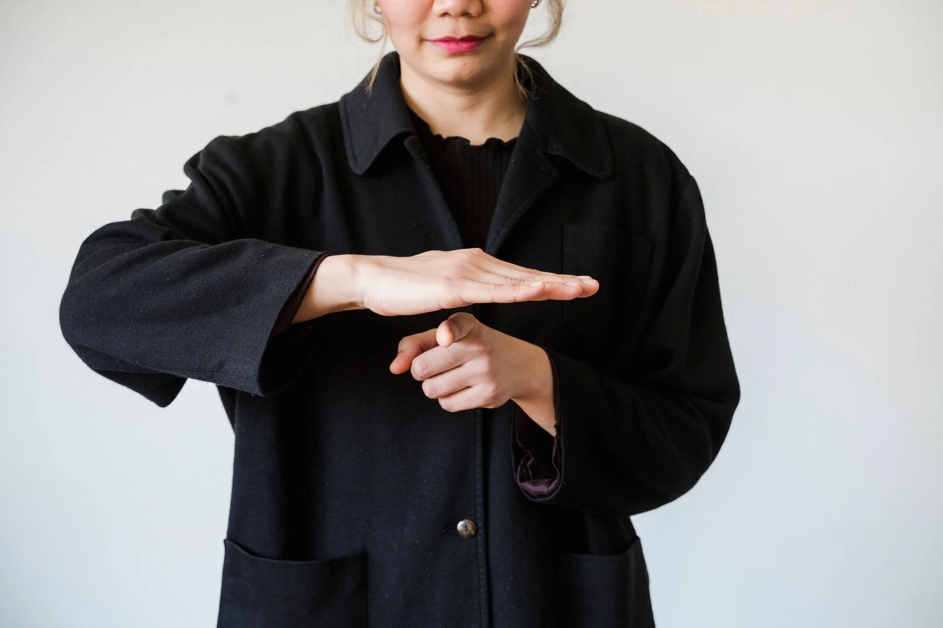 Femme en manteau noir effectuant un geste de langue des signes sur fond blanc