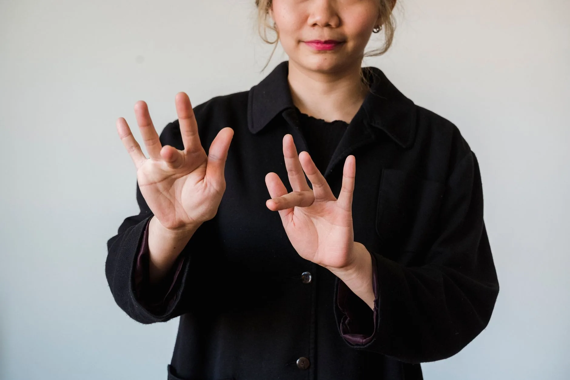 Femme en veste noire levant les mains pour former un signe de la langue des signes