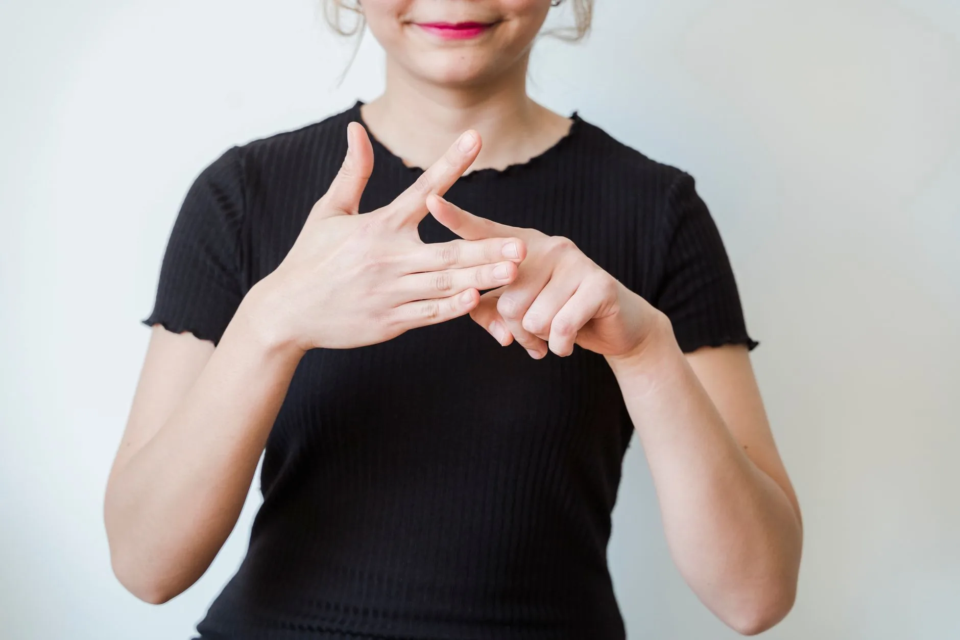 Femme souriante en haut noir faisant un geste des mains devant sa poitrine sur fond blanc