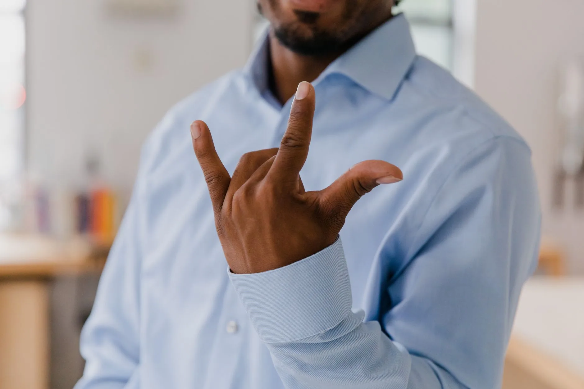 Homme en chemise bleue effectuant un geste de langue des signes en intérieur
