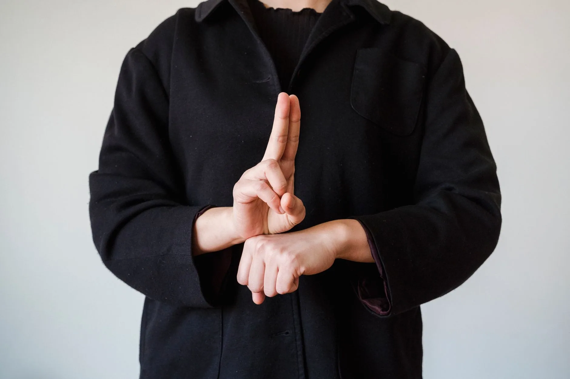 Personne en manteau noir formant un geste de langue des signes devant un fond blanc