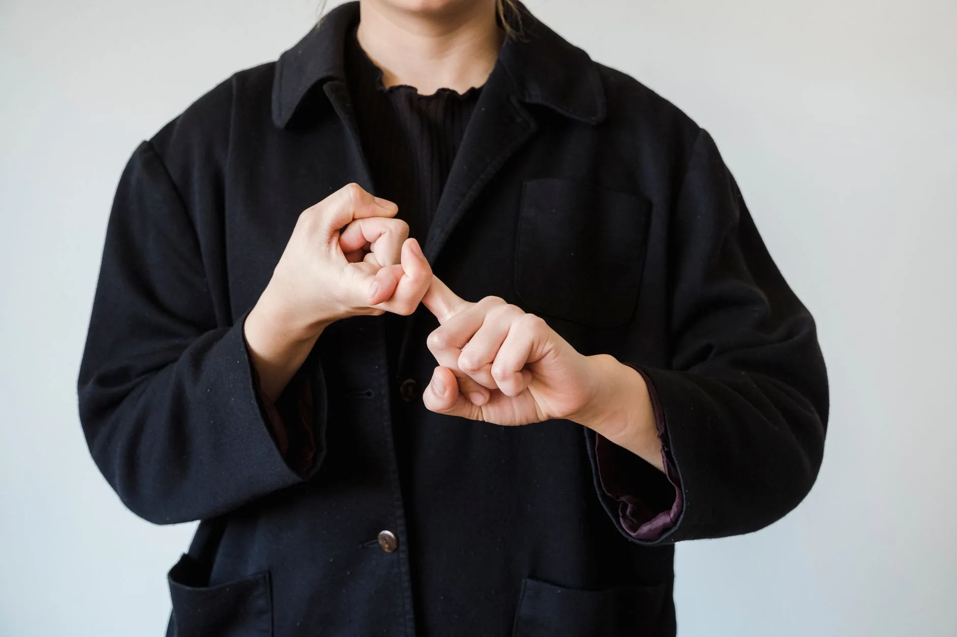 Personne en veste noire effectuant un geste de langue des signes sur fond blanc