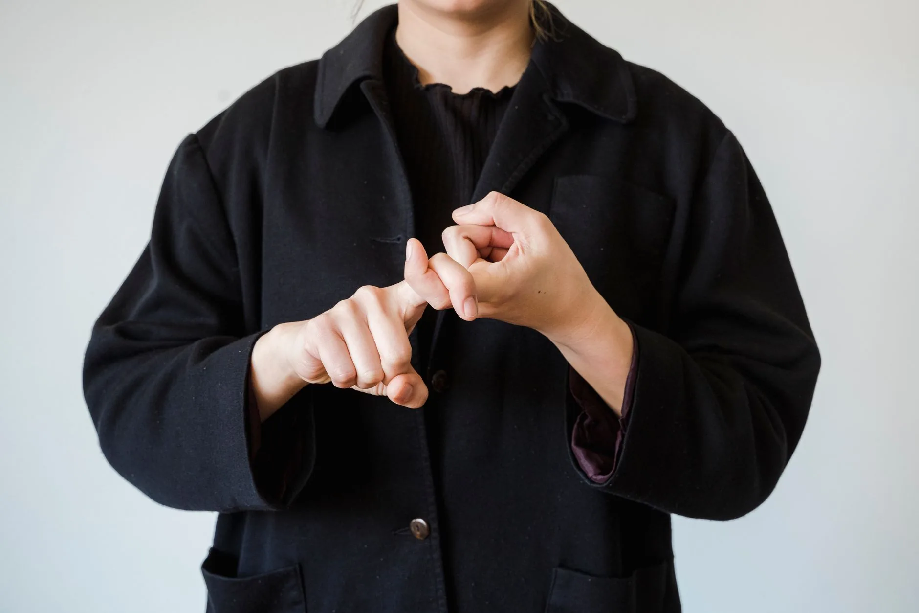 Personne en manteau noir formant un geste de langue des signes sur fond clair